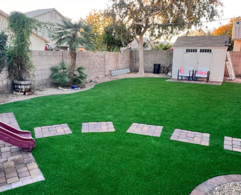 Artificial turf backyard with stepping stones, slide, and shed