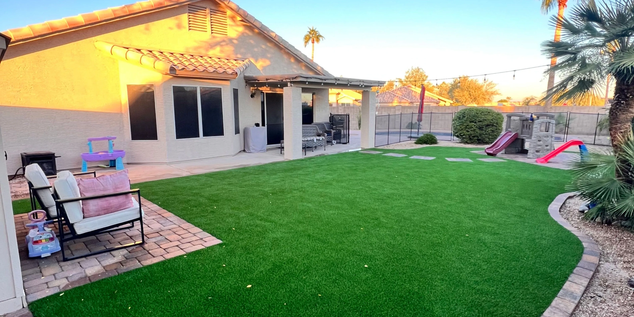 Backyard with green lawn, patio seating, and kids’ play area
