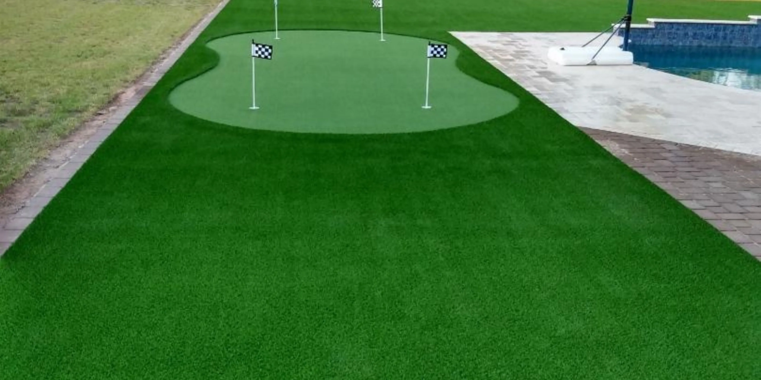 Backyard artificial turf putting green installed beside pool patio