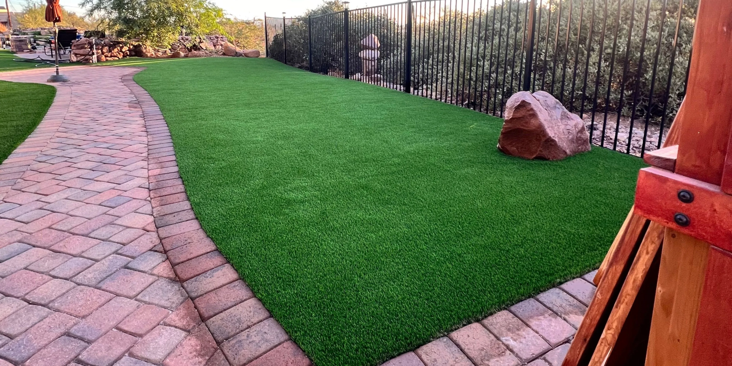 Curved brick pathway next to artificial grass and a rock