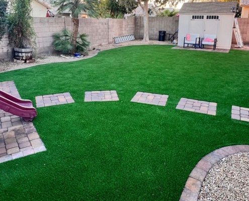 Backyard with artificial grass, stepping stones, a small slide