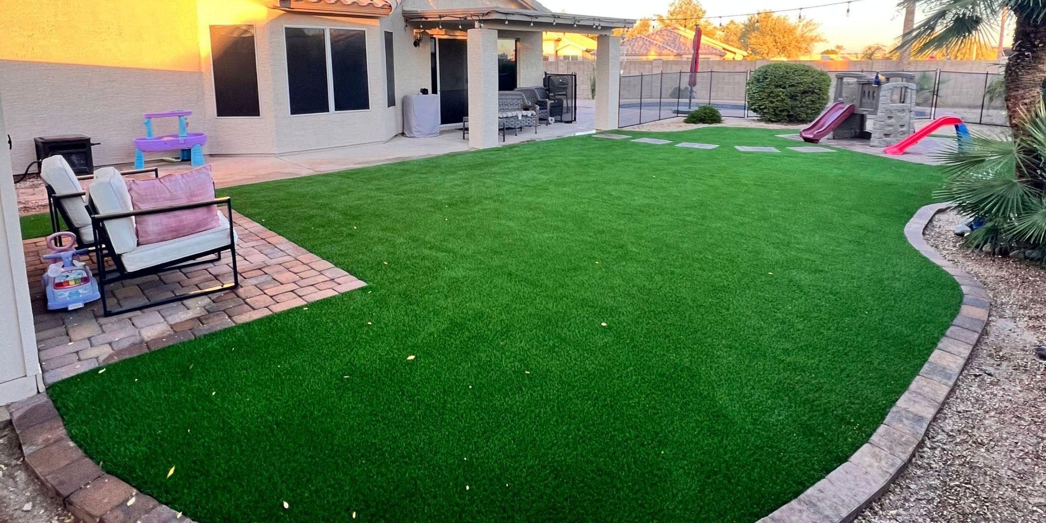 Backyard with lush artificial grass and patio seating 
