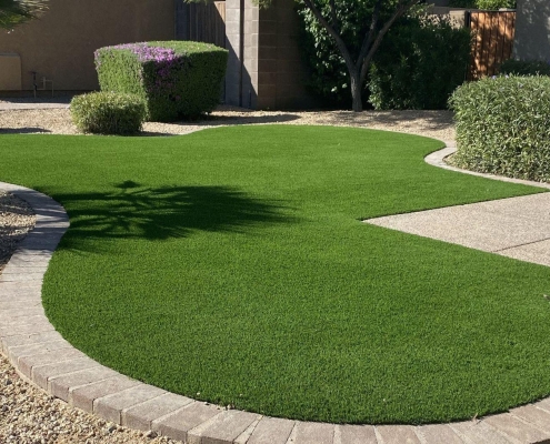 Curved artificial grass lawn bordered by stone pavers